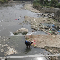 A poor man collecting/cleaning food in a dirty, lifeless and stinky river